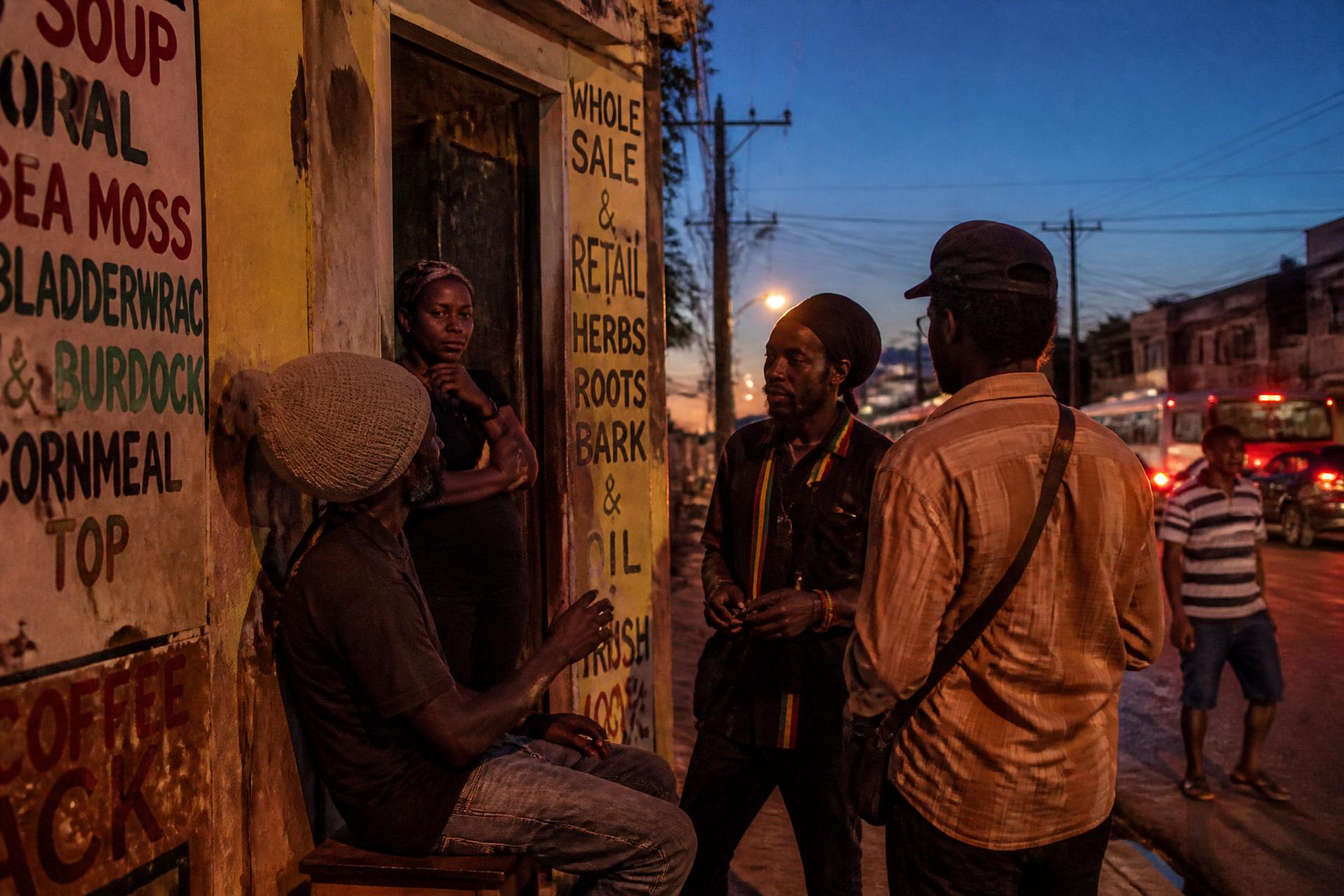 People talking outside a hand-painted shopfront on a Kingston street at dusk